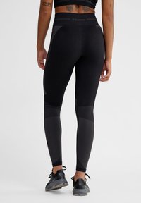 Svarta leggings med texturerade paneler och hög midja, tillverkade av stretchigt tyg. Accentuerade med subtil branding och kontrasterande nyanser.