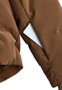 Smešasta smeđa jakna s punjenjem, glatke teksture, s džepom na rukavu sa zatvaračem koji djelomično otkriva bijelu karticu unutar njega.