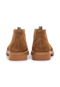 Bottines en daim marron avec des orteils arrondis et une semelle en caoutchouc robuste. Comprend une languette rayée et des coutures le long du bord de la semelle.