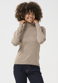 Maglione a collo alto beige con maniche lunghe e polsini a coste, realizzato in un materiale morbido, abbinato a jeans blu scuro.
