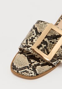 Python-print slide-sandaal met een brede band, een gouden rechthoekige gesp, gestructureerd faux leer en een platte, bruine zool.