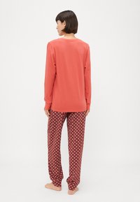 Rode lange mouw top gecombineerd met losse pyjamabroek met een patroon van diamanten in tinten roze op een donkerrode achtergrond.