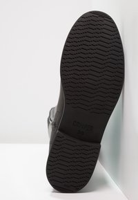 Suela de zapato negra con un diseño de dibujo, que presenta el texto "CAMPER 36." El material parece ser goma con un acabado suave.