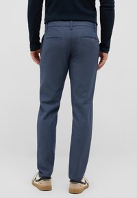 Niebieskie spodnie o teksturowanej powierzchni z tylnymi kieszeniami, noszone z beżowymi butami. Charakteryzują się delikatnym wzorem i dopasowanym krojem, co zapewnia elegancki wygląd.