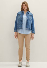 Jeansjacka med knäppning framtill, två bröstfickor och en medelblå tvätt, kombinerad med en ljusblå skjorta och beige byxor.