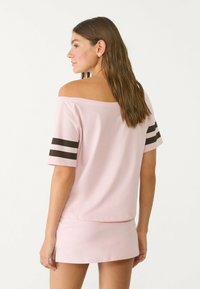 Roze off-the-shoulder top met korte mouwen en zwarte strepen. Soepele stof met een relaxte pasvorm, gecombineerd met een bijpassende rok.