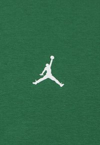 La tela de algodón verde presenta un destacado logo bordado en blanco del Jumpman, que representa una figura en el aire con un baloncesto.