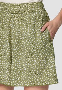 Zielona spódnica z teksturowanej tkaniny, z białym wzorem w kropki, elastycznym paskiem w talii oraz kieszeniami bocznymi.