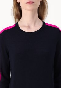 Ναυτικό μπλε πουλόβερ με ροζ τόνους στους ώμους, στρογγυλή λαιμόκοψη και απαλή υφή. Η κοντινή λήψη επισημαίνει την αντίθεση χρωμάτων και τα στοιχεία σχεδίασης.