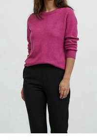 Fuchsiastrumpa med rund halsringning och ribbad manschett, i kombination med svarta tajta byxor. Enkel design med en mjuk textur.