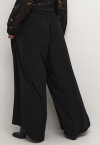 Pantalons larges noirs avec une ceinture élastique, présentant une texture lisse et un matériau doux. Convient pour diverses occasions.