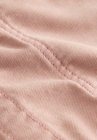 Tissu rose pâle avec de fines rayures verticales, affichant une texture douce. Une couture visible longe le bord, mettant en avant le savoir-faire.