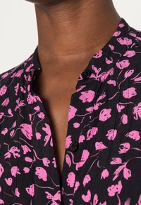 Top in tessuto nero con motivo floreale rosa, patta con piccoli bottoni neri e colletto alla mandarina con dettagli a plissettatura.