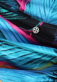 Colorful fabric showcasing a blend of turquoise and black with pink accents. Features stitching details and a circular silver tag.