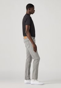 Jeanși gri cu croială dreaptă și o etichetă din piele pe spate. Asociați cu un tricou negru și adidași albi. Design simplu, stil casual.
