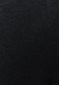 Närbild av svart stickad tyg med synligt ludd och fina fibrer på ytan.