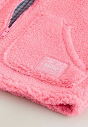 Růžová fleecová bunda s texturovaným, nadýchaným povrchem. Má zip, kapsu na břiše a látkovou cedulku s nápisem "Monza, Itálie".