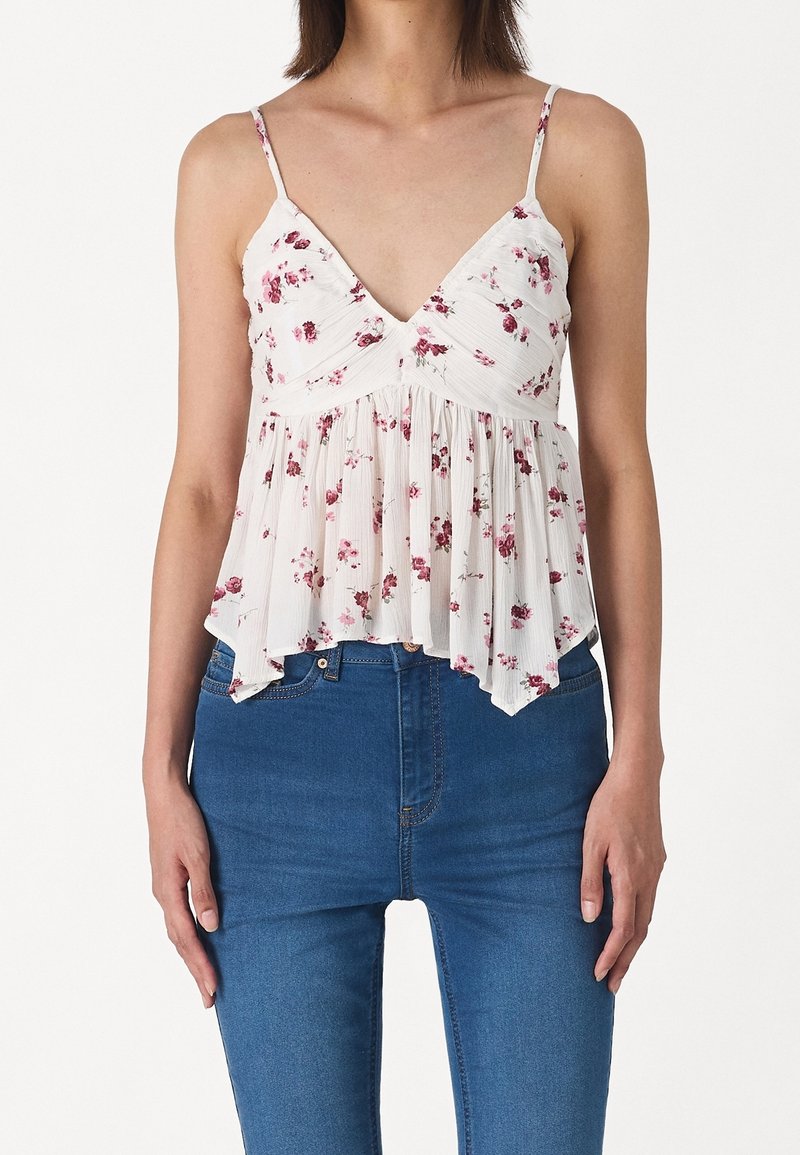 Top senza maniche in tessuto di un leggero crema con stampa floreale, dotato di scollatura a V, corpetto arricciato e orlo svasato. Abbinato a jeans blu.