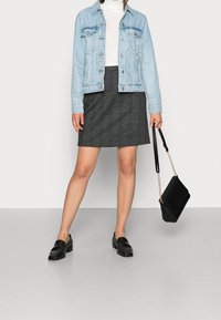 Chaqueta de denim de color azul claro, suéter blanco de cuello alto, falda gris, mocasines negros, sosteniendo un bolso negro con cadena dorada. Tela suave y diseño clásico.