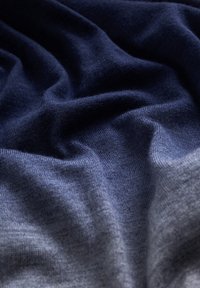 Tissu tricoté doux avec une texture lisse, présentant un dégradé de bleu marine foncé à gris clair, délicatement plié avec des motifs de tissage visibles.