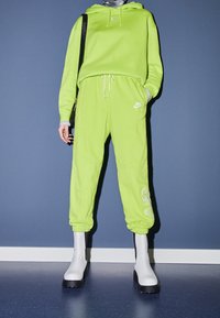 Neongrön Nike-hoodie och matchande joggers med logodetaljer, parat med vita ankelhöga stövlar med en kraftig svart sula.