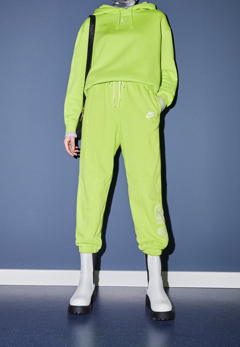 Neongrön Nike-hoodie och matchande joggers med logodetaljer, parat med vita ankelhöga stövlar med en kraftig svart sula.