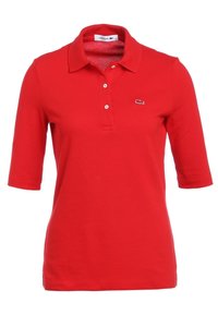 Červené polo tričko s krátkým rukávem a límečkem, se třemi bílými knoflíky a malým vyšitým krokodýlovým logem na levé hrudi.