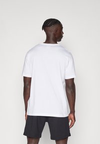 T-shirt en coton blanc à manches courtes, coupe droite et col rond, associé à un short noir. Design minimal, texture lisse.