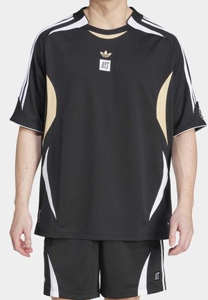 Personne portant une tenue de sport Adidas noire avec des bandes blanches et des accents beige, avec le logo NTS sur le t-shirt et le short.