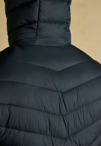 Czarna pikowana kurtka z kapturem, zbliżenie na tył pokazujące szew w kształcie chevronu i subtelne logo marki "Joules".