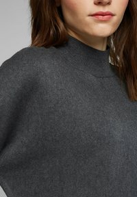 Donkergrijze trui met hoge nek, gemaakt van zacht materiaal met een gladde textuur en geribbelde kraag. Close-up van de halslijn en het schoudernaad.