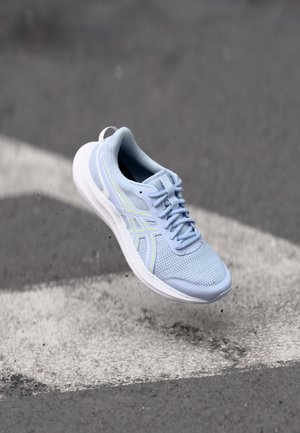 Baskets athlétiques bleu clair avec semelle blanche flottant au-dessus d'un trottoir gris avec des marquages blancs.