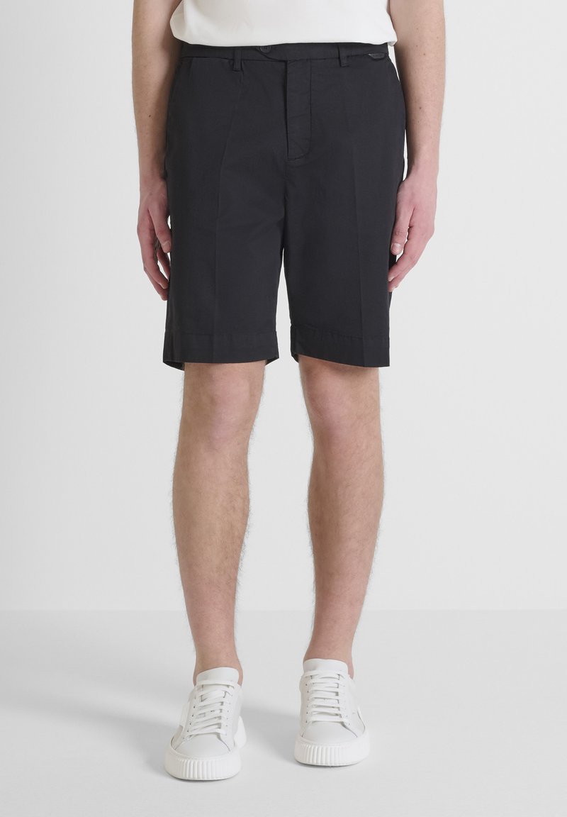 Pantaloni corti neri con un design su misura, tessuto leggero, tasche laterali e una texture liscia, abbinati a sneakers bianche.