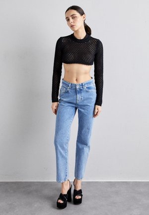 Svart kortermet langermet topp med mesh mønster, kombinert med lyseblå høytliv jeans og svarte platåsandaler.