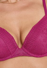 Reggiseno in pizzo magenta con design a V, caratterizzato da motivi floreali, spalline regolabili e una consistenza morbida.