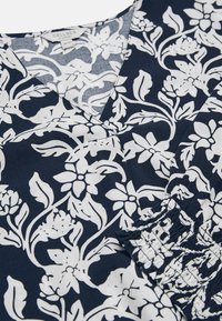 Marineblauw kledingstuk met wit bloemenpatroon, V-hals en elastische mouwzoom met plooien.