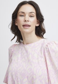 Vaaleanpunainen mekko, jossa on teksturoidut kankaat, hienovarainen kuvio ja puffi hihat. Pyöreä pääntiellä on yksinkertainen ja tyylikäs.