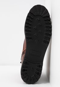 Brun läderstövel med en texturerad svart gummisula. Har ett robust mönster och logodetalj på sules yta.