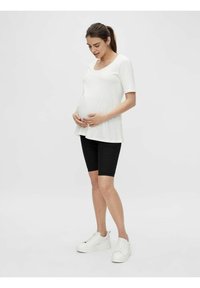 Maglietta a maniche corte per la maternità in tessuto bianco abbinata a pantaloni corti neri e sneakers bianche, con vestibilità comoda e colletto rotondo.