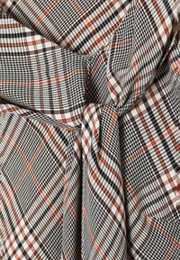 Mustvalge ruuduline kangas, millel on oranž tooni aktsendid, triibuline viimistlus ja sõlmekujundus, mis demonstreerib tihedat ja lõdvestunud kude.