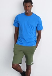 Blå bomulds t-shirt med rund hals, parret med grønne shorts med et hvidt logo. Sættet er enkelt og afslappet.