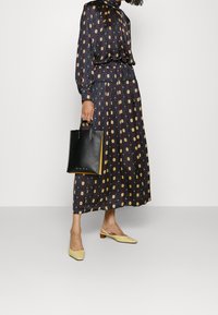 Musta kuvioitu maksimekko, jossa on pyöreitä motiiveja, pitkät hihat ja koottu vyötärö. Musta käsilaukku, jossa on lyhyet kahvat ja keltaiset yksityiskohdat. Keltaiset slingback-kengät.