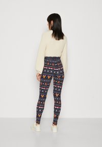 Strikkede leggins med marineblå bakgrunn som har et vintermønster med snøfnugg, pepperkakemenn og festlig tekst. Kombinert med en kremfarget genser.