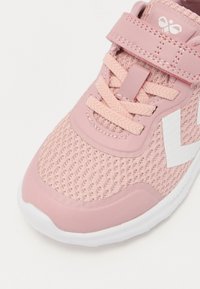 Roze kindersneaker met mesh bovenwerk, klittenbandriem, veters, witte zool en wit chevron-logo aan de zijkant.