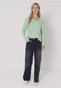 Ljusgrön, ribbad stickad tröja med V-ringning, kombinerad med mörka denimbyxor med vida ben och vita sneakers. En enkel, avslappnad outfit med en ledig passform.