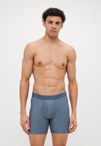Herrebokser i blågrått stoff, med en teksturert overflate og en bred elastisk linning med "YOUR UNDER" preget.