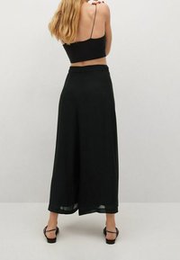 Zwarte wijde broek met een vloeiende uitstraling en een elastische tailleband. De stof heeft een soepele textuur en valt elegant tot aan de enkels.