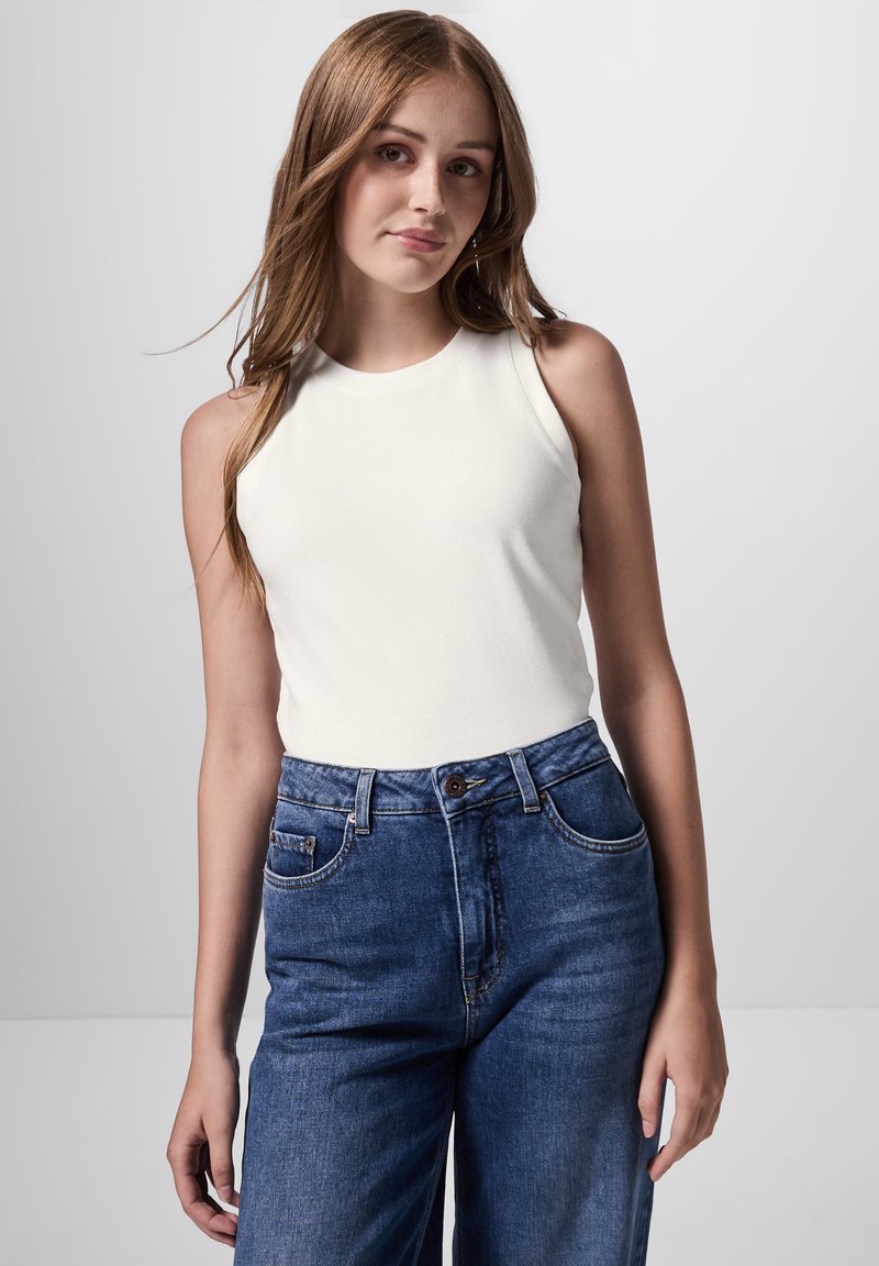 Witte mouwloze top gecombineerd met high-waisted blauwe denim jeans, met een klassieke vijf-pocket ontwerp en een standaard knoopsluiting.
