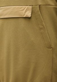 Κοντινή λήψη φούστας από υφή καφέ χακί ύφασμα με πλαϊνή τσέπη και επάλληλη λεπτομέρεια στη μέση.