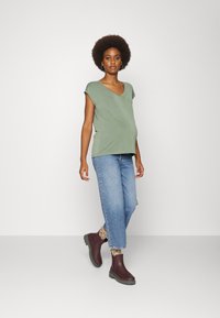 T-shirt verde com decote em V, de corte solto, combinado com jeans de perna reta de tom azul claro e botins escuros burgundy com solas grossas.